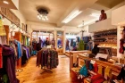 A stylish interior view of the Chapati Design store with an elegant, patterned chaise longue in the center. All around, sustainable garments are hung on rustic wooden shelves. Warm lighting and wooden floors create an inviting atmosphere.