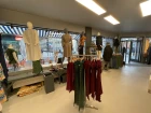 The spacious sales area of Chapati Design with modern ceiling lamps. In the middle is white furniture with folded clothes, surrounded by clothes rails with colorful patterns. In the background are changing rooms, a mirror and a wall decoration with a picture of people in sustainable clothing.