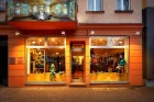 Exterior view of the Chapati Design store in Schönhauser Allee, Berlin-Prenzlauer Berg. The shop windows are warmly lit and display sustainable fashion on mannequins as well as decorative elements. Above the store is a large banner with an artistic motif of a historic building.