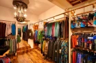 Bright and spacious sales area by Chapati Design with wooden flooring and stylish lighting. Colorful garments hang on metal clothes rails along the walls, while central clothes racks display other fashions. A decorative mannequin in sustainable clothing stands at a decorative sales counter.